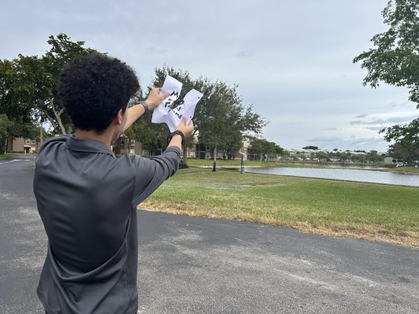 By a lake, a boy rips a paper that reads “My Good Friend” in half.